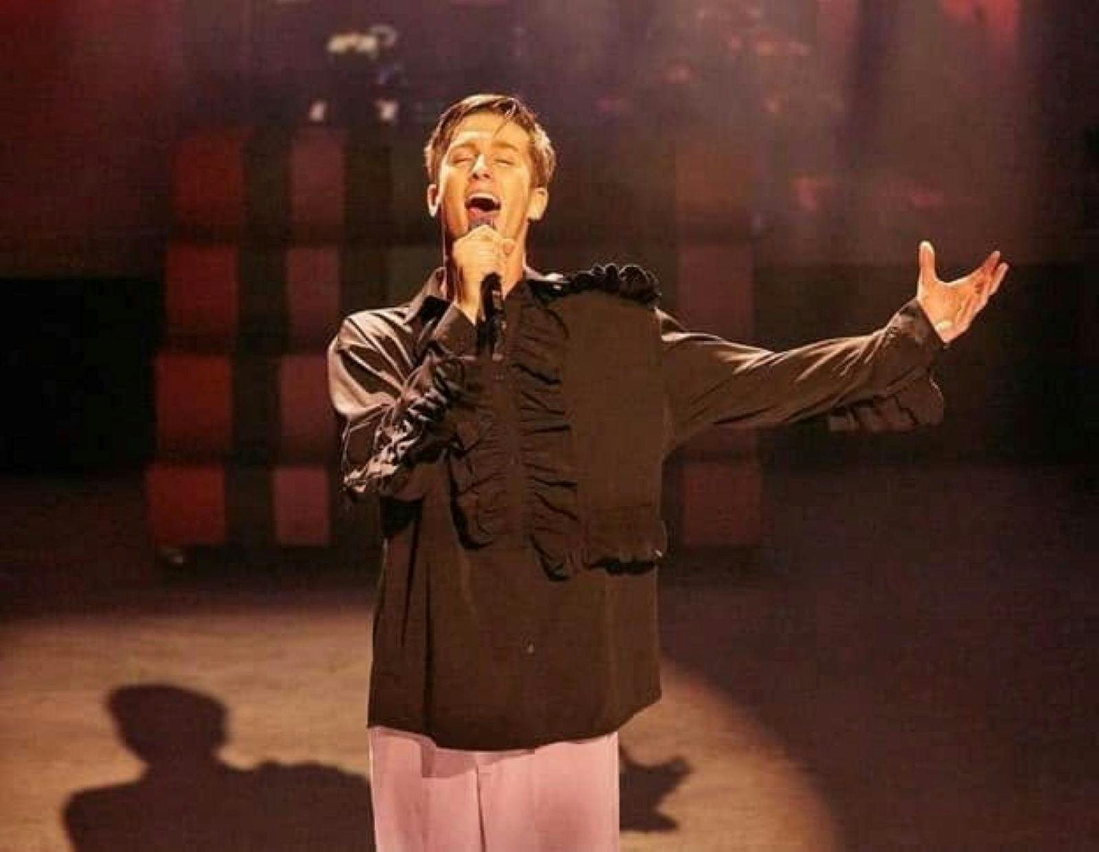 A man singing into a microphone with his left arm outstretched.