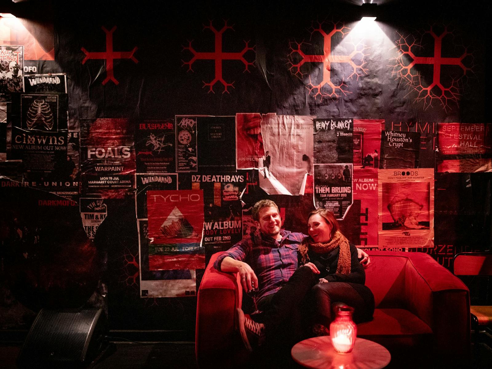 A man and a woman sitting on a couch laughing by candlelight in Altar's red-lit lounge bar