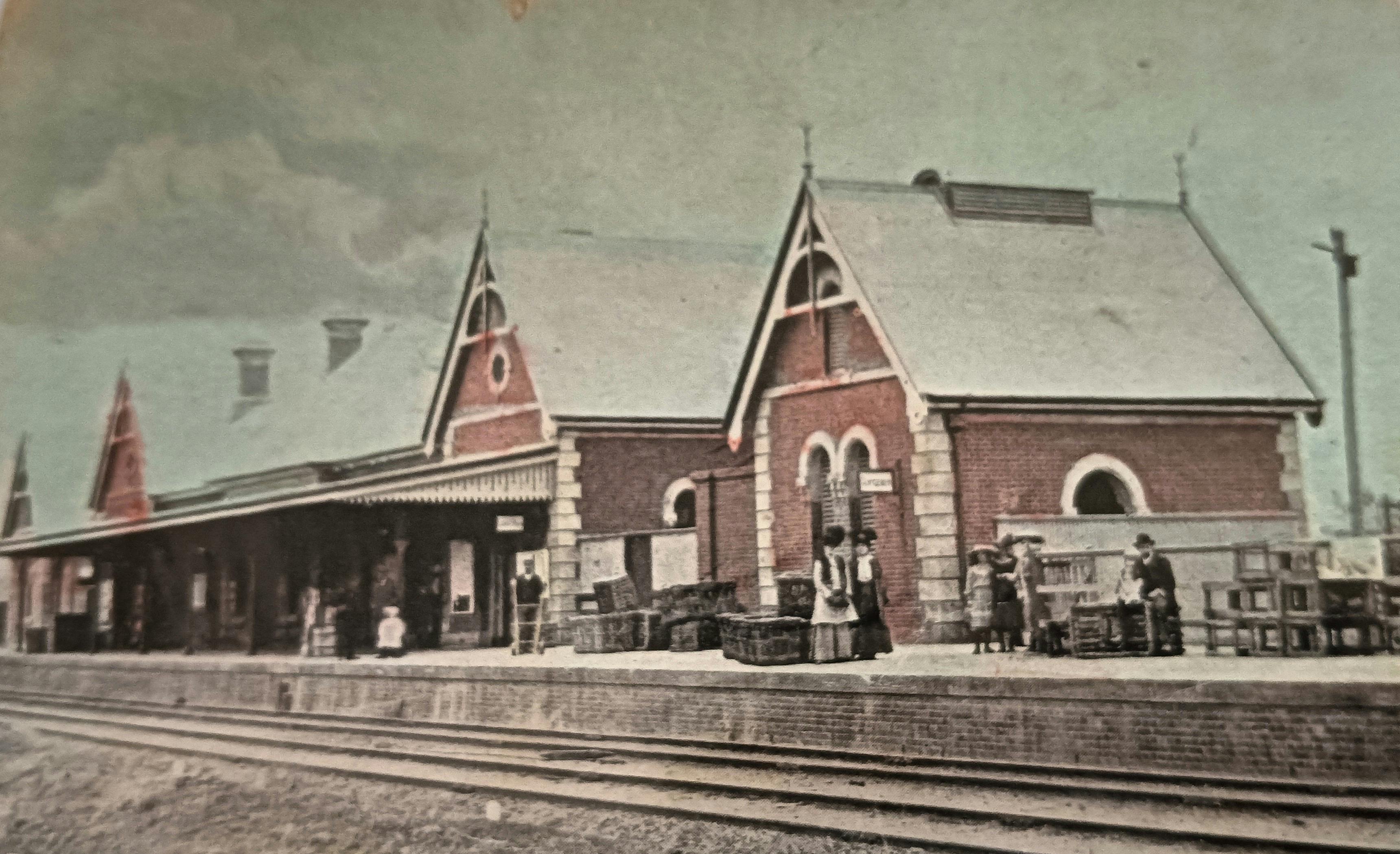 Hand coloured photograph of Young Railway Station showing people standing on the platform.