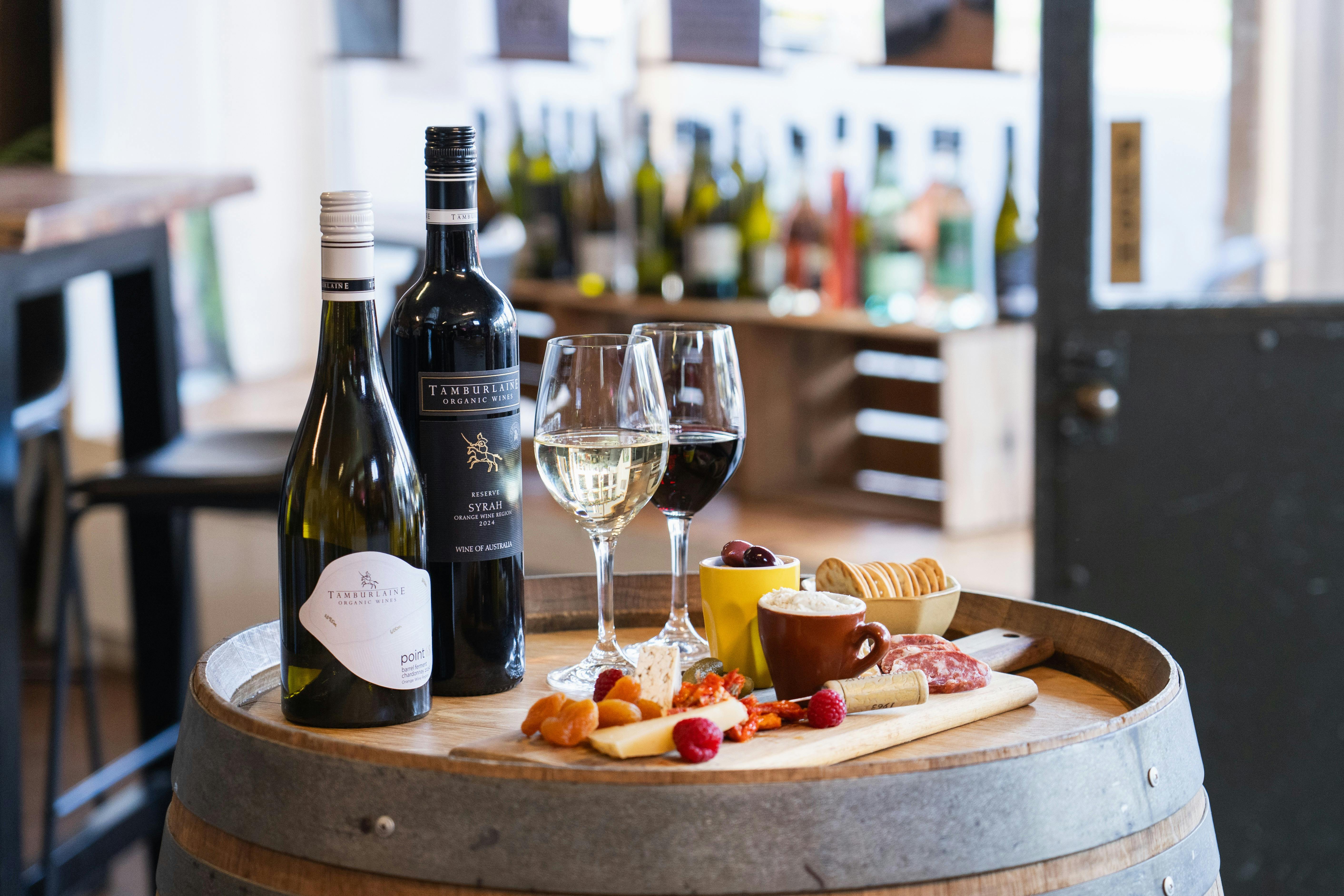 Two bottles of wine, two glasses of wine and a charcuterie plate on a barrel