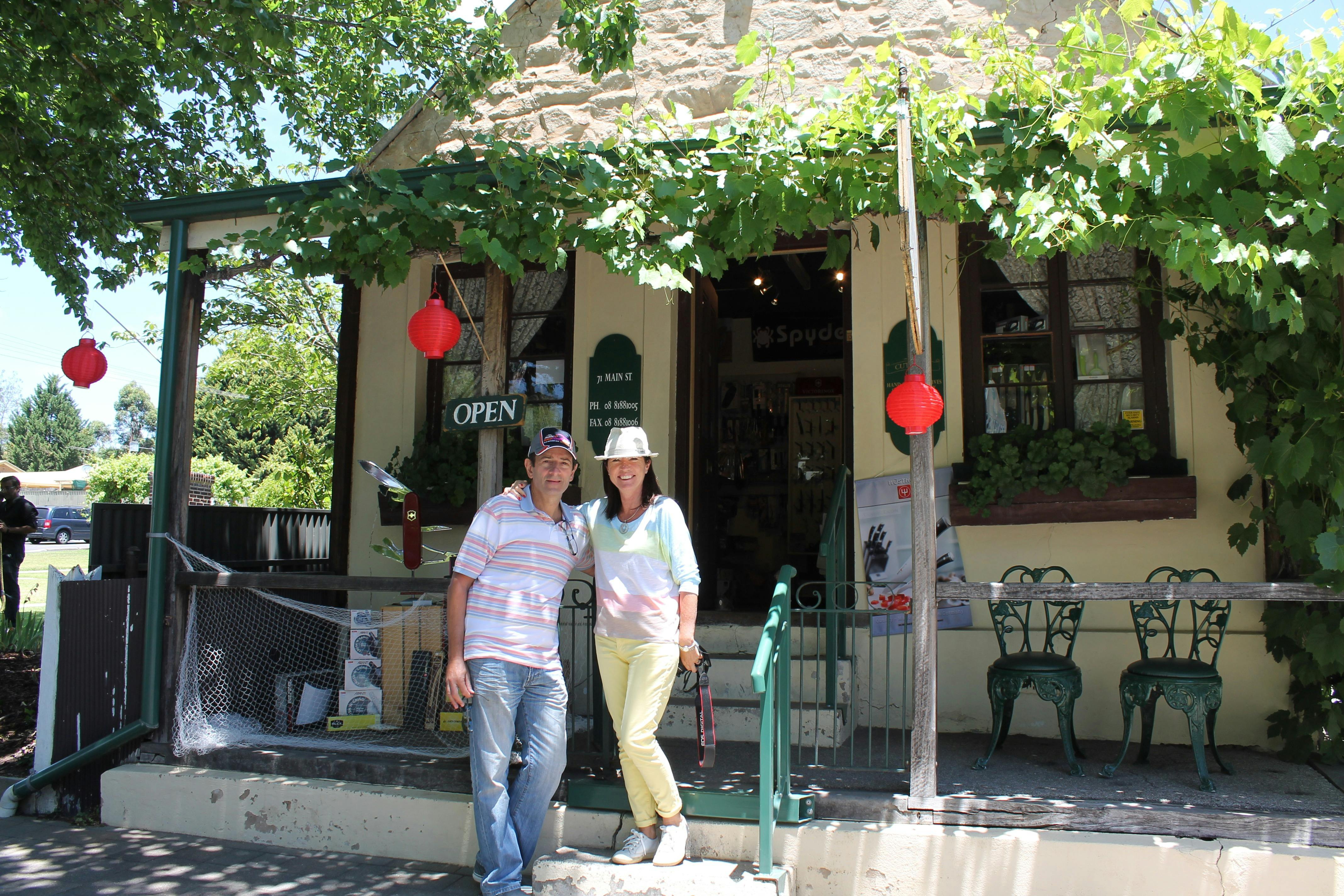 A couple standing outside an old shop with grape vines on the verandah