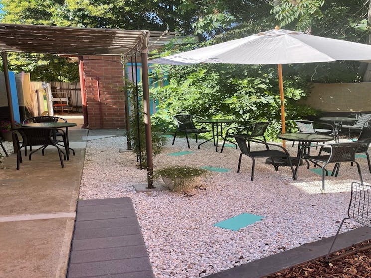 Outdoor dining area with an open umbrella and black chairs and tables. There is rocks and pavers
