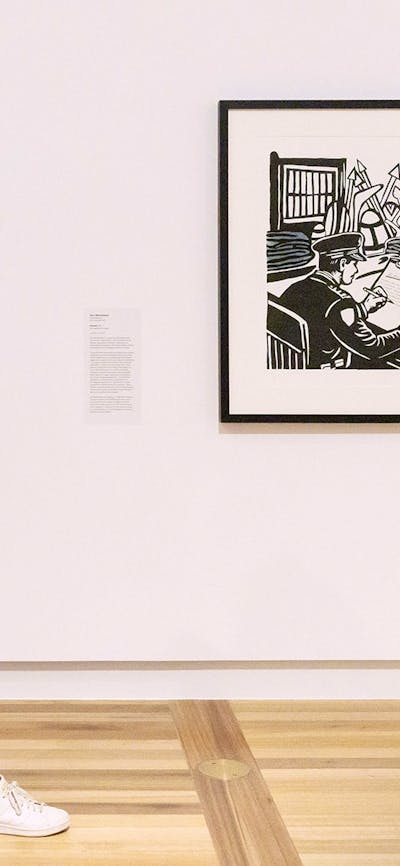 A person wearing a pink dress walks by a Gallery wall, looking at several artworks.