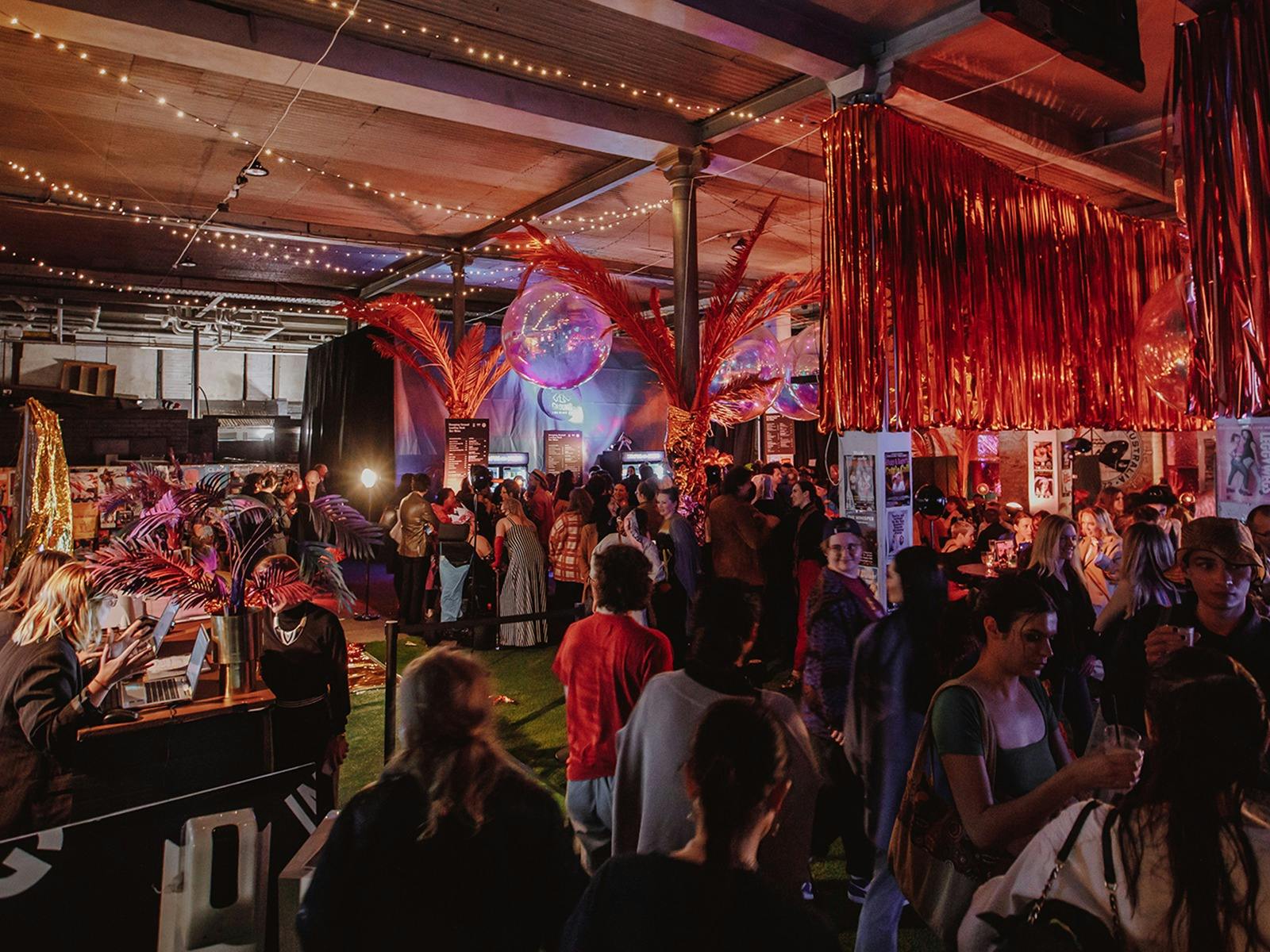 A crowd gathers underneath fringed decorations at the pop-up bar inside Festival Hub: Trades Hall