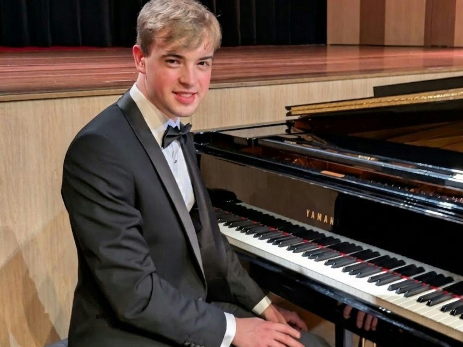 Luke Bowen sits at a grand piano at Bowral Memorial Hall. He is a young man wearing a tuxedo.