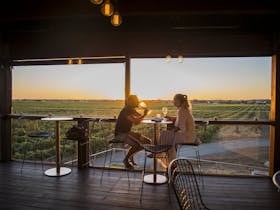 A couple enjoying a glass of wine and the view of vineyards and the sunset