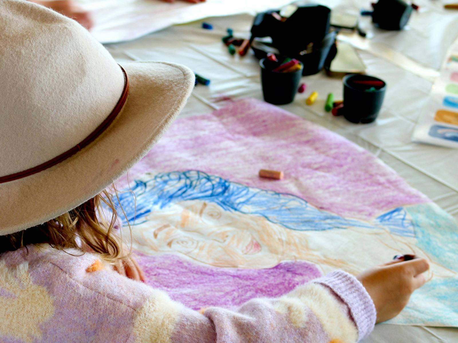 A young girl wears a felt hat, looking at a bright colourful artwork on her kite