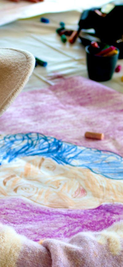 A young girl wears a felt hat, looking at a bright colourful artwork on her kite