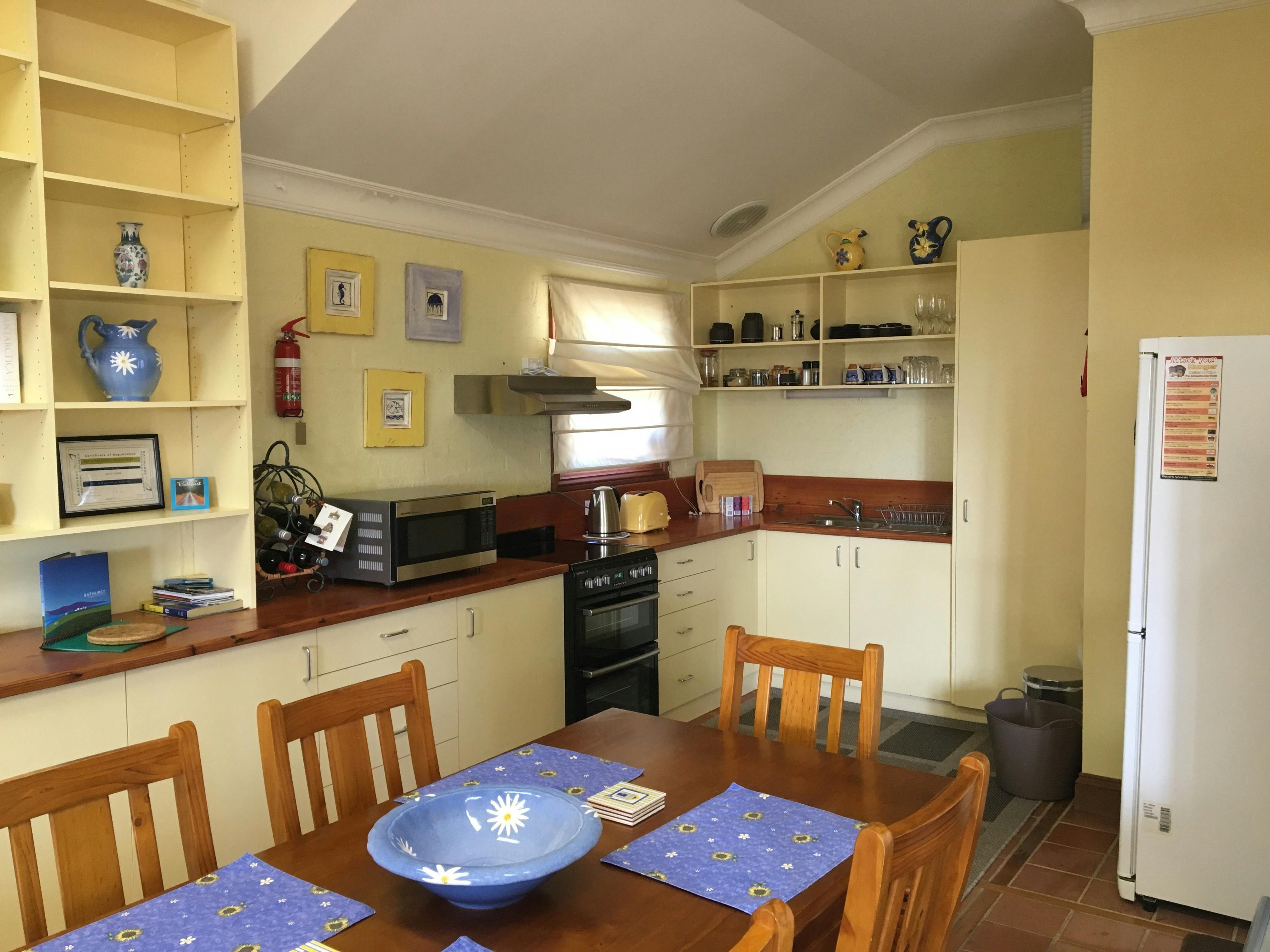 Photo shows the dining table and chairs with the kitchen facilities in background
