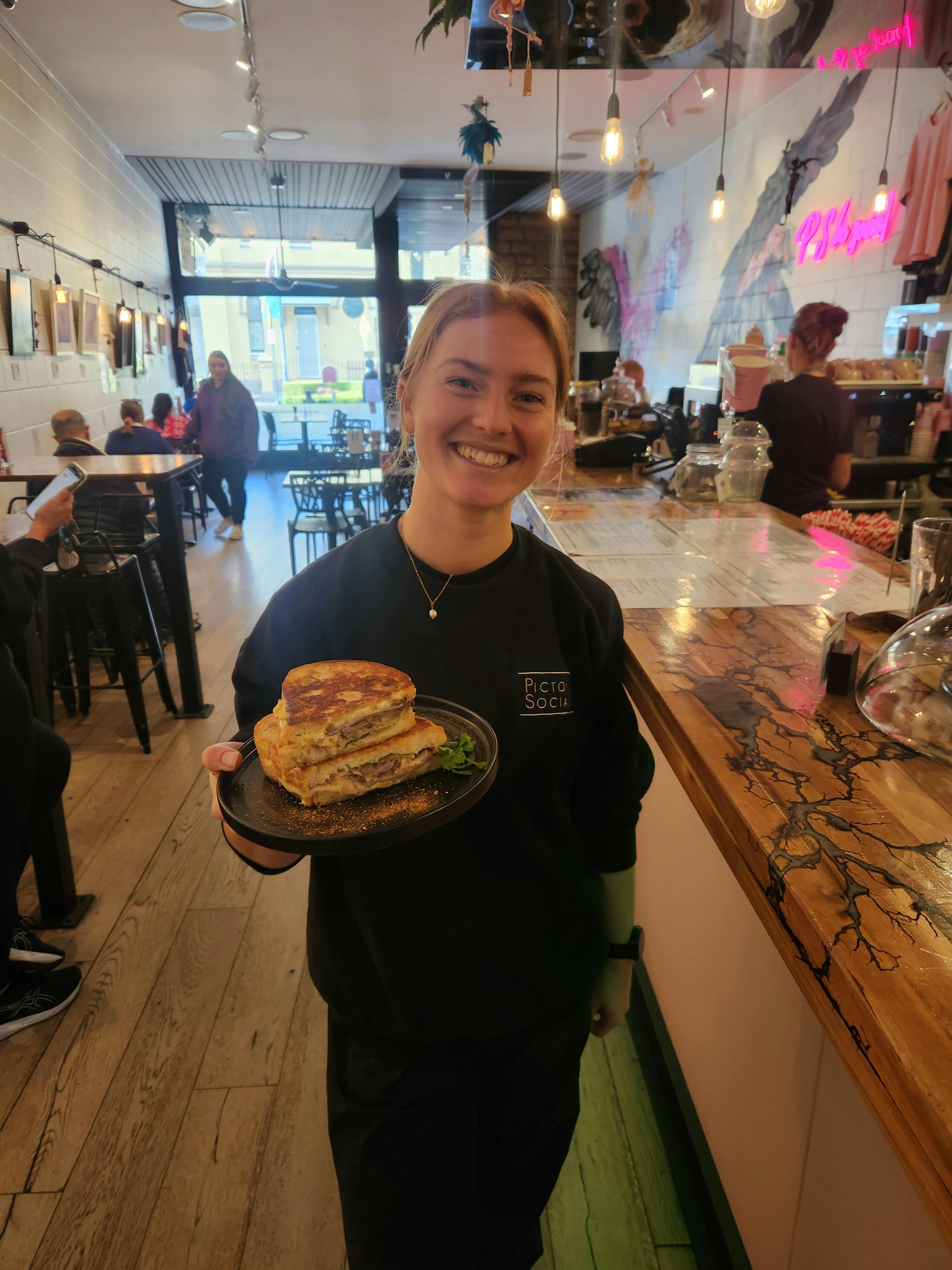 A photo of Gillian holding the reuben sandwich special standing in picton social cafe