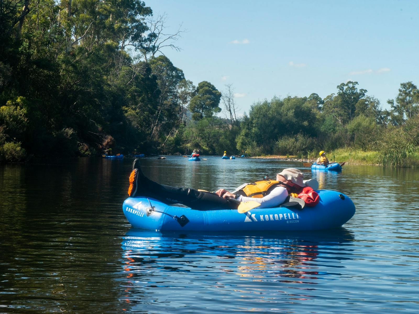 A packrafter reclines, asleep while floating down a river in Tasmania