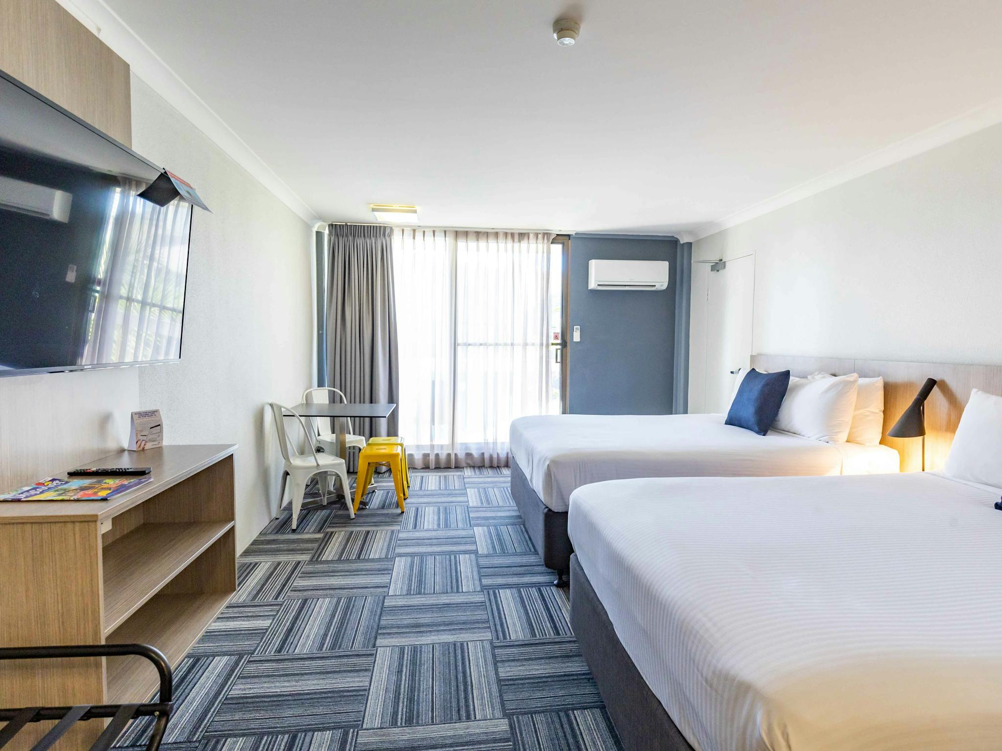 Two double beds in a room with a glass door overlooking a balcony and also a TV mounted on a wall. Two double beds in a room with a glass door overlooking a balcony and also a TV mounted on a wall.