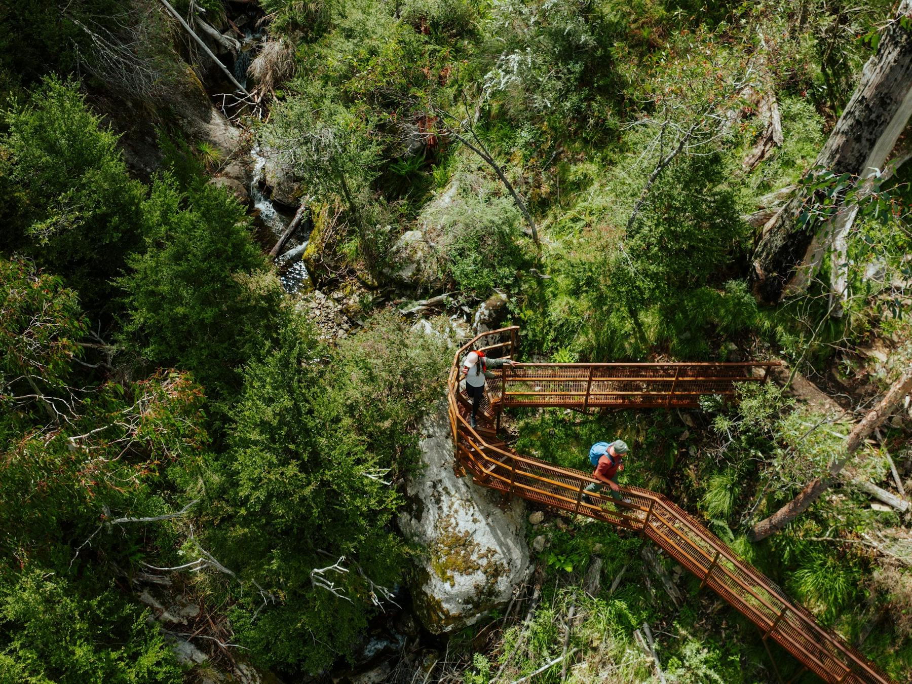 Two hikers crossing a metal bridge on a walk in Kosciuszko National Park.
