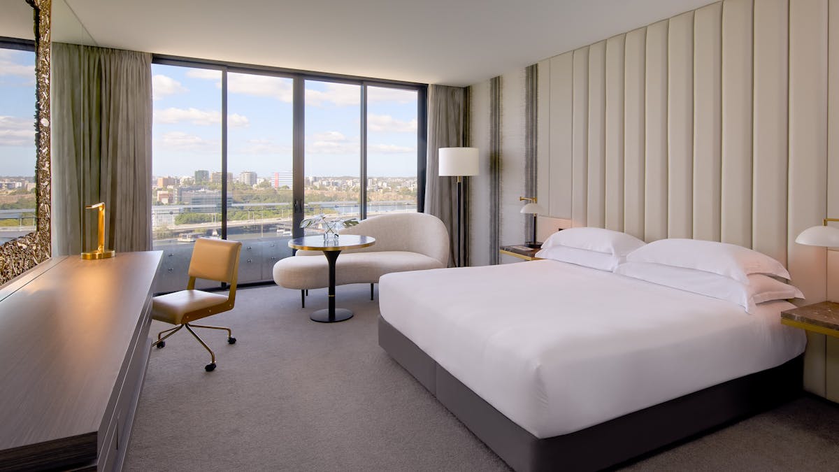 Modern hotel room with king bed, curved sofa and desk overlooking wide city views