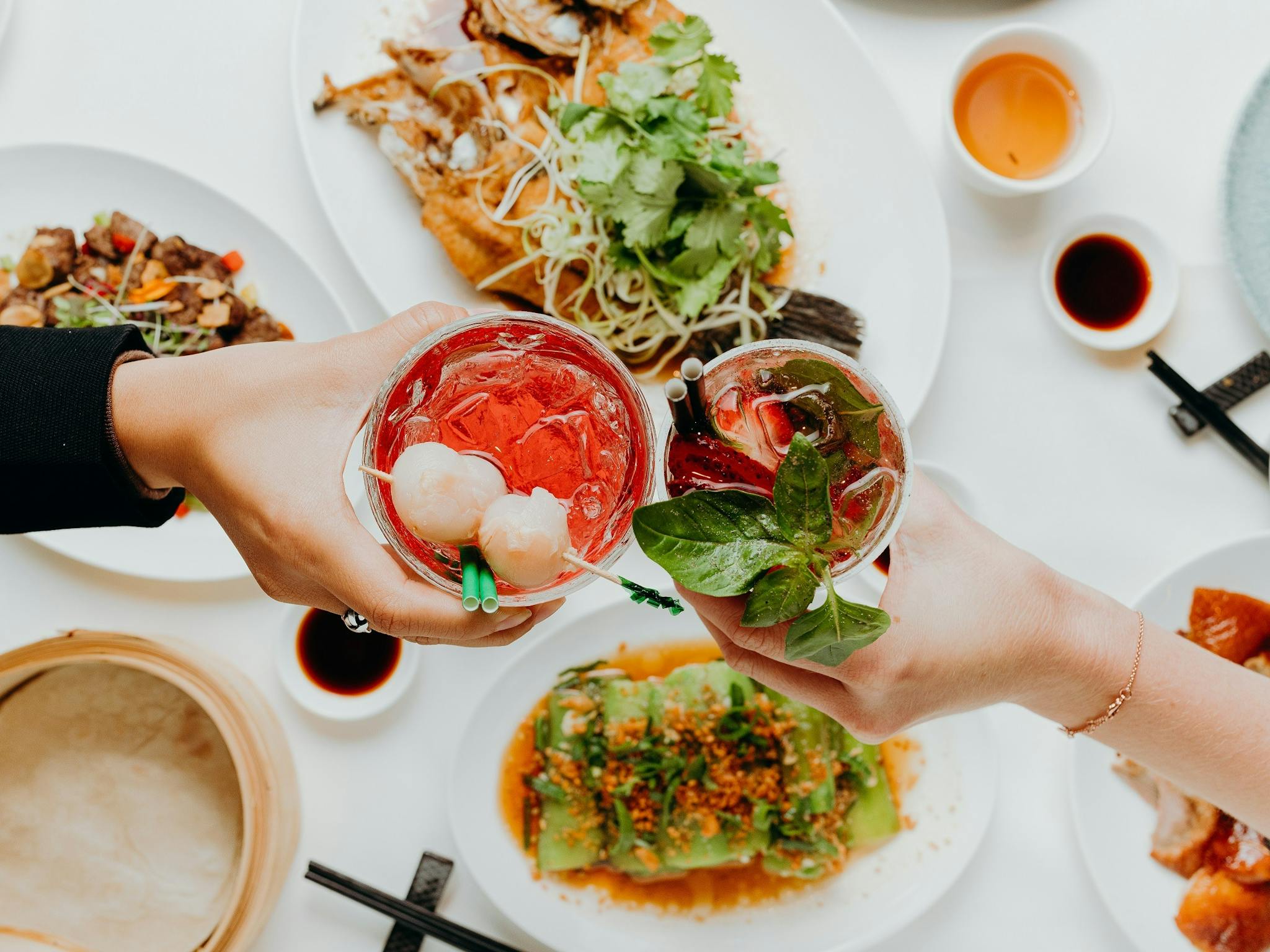Two people hold two drinks above a spread of food. Two people hold two drinks above a spread of food.