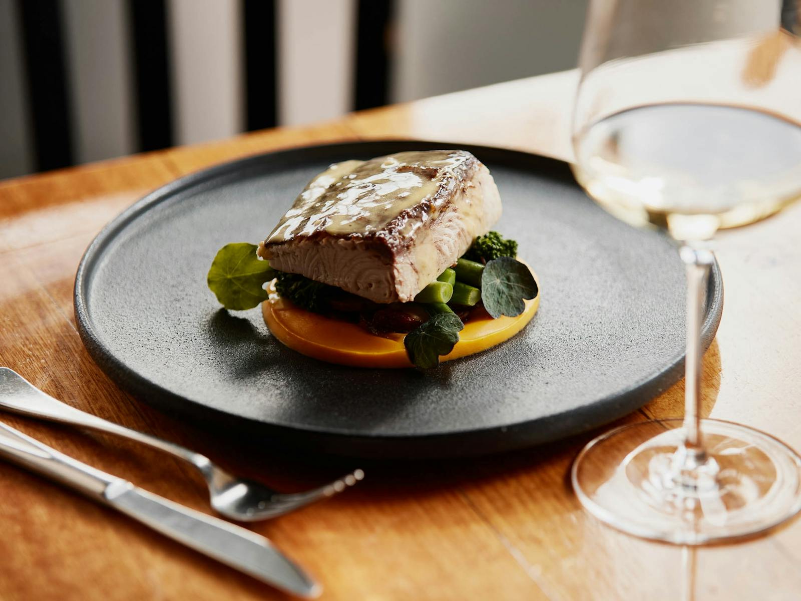 A plate with a cut of wild fish fillet sitting on a bed of greens and pumpkin puree
