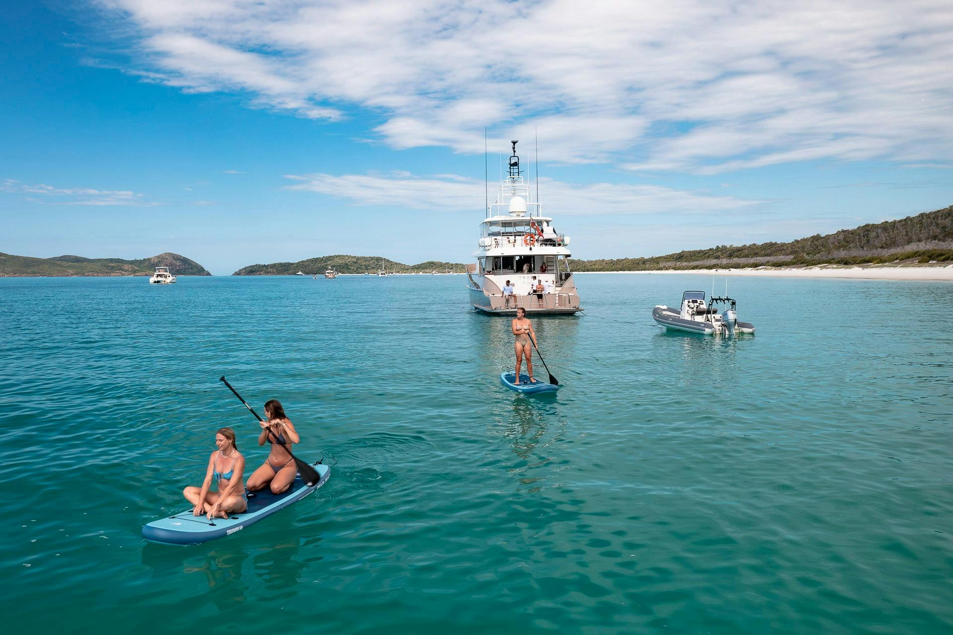Paddle boarders next to Whitehaven Beach with Texas T motor yacht