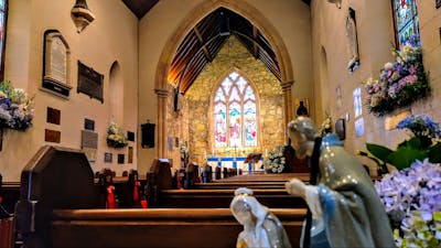 Stained glass window inside stone church with wooden pews and colourful flowers