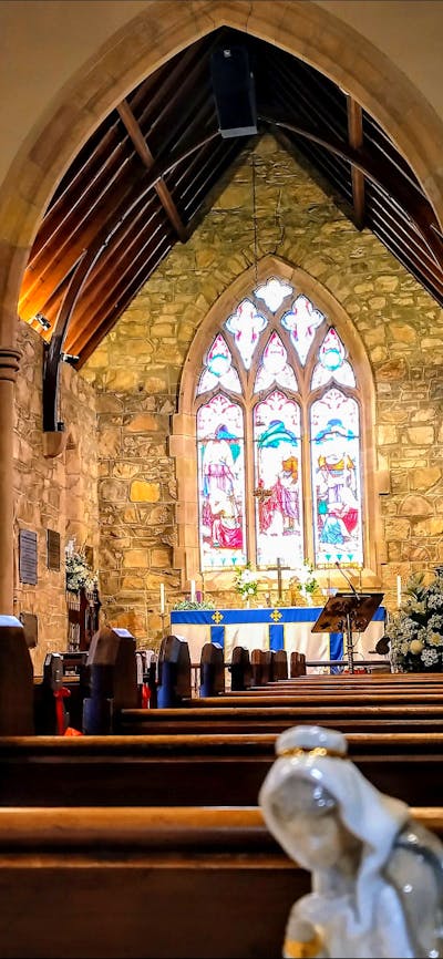 Stained glass window inside stone church with wooden pews and colourful flowers