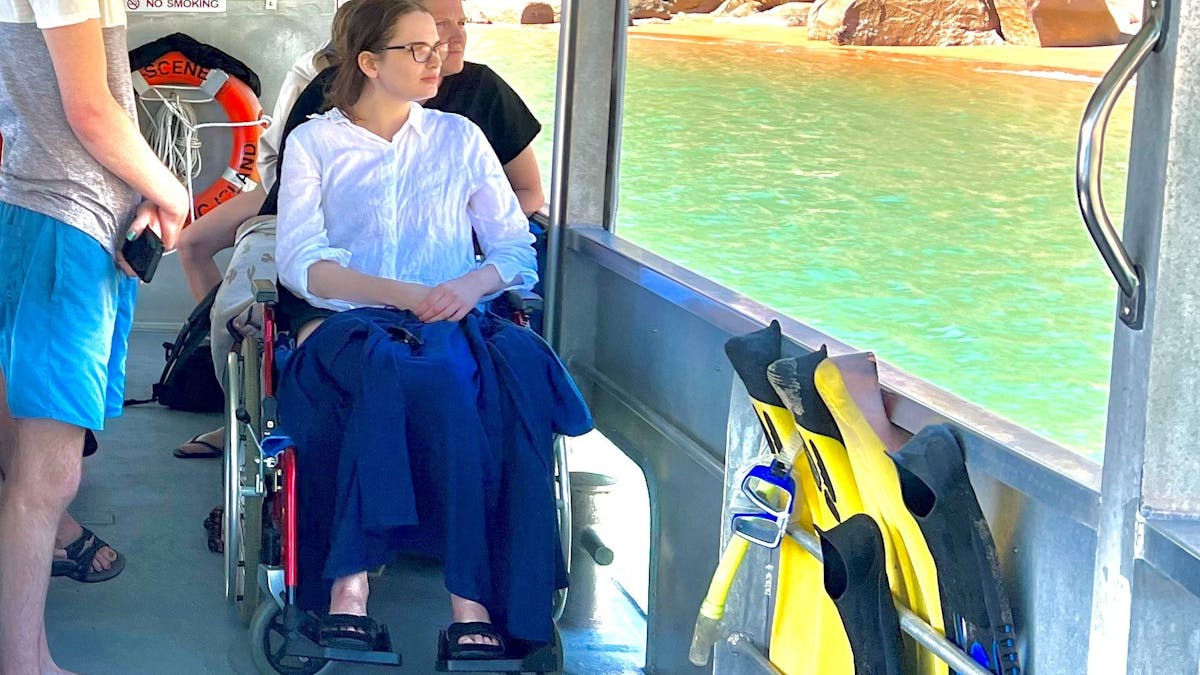 guests onboard boat with lady in wheelchair looking out at beautiful tropical beach and sunny day