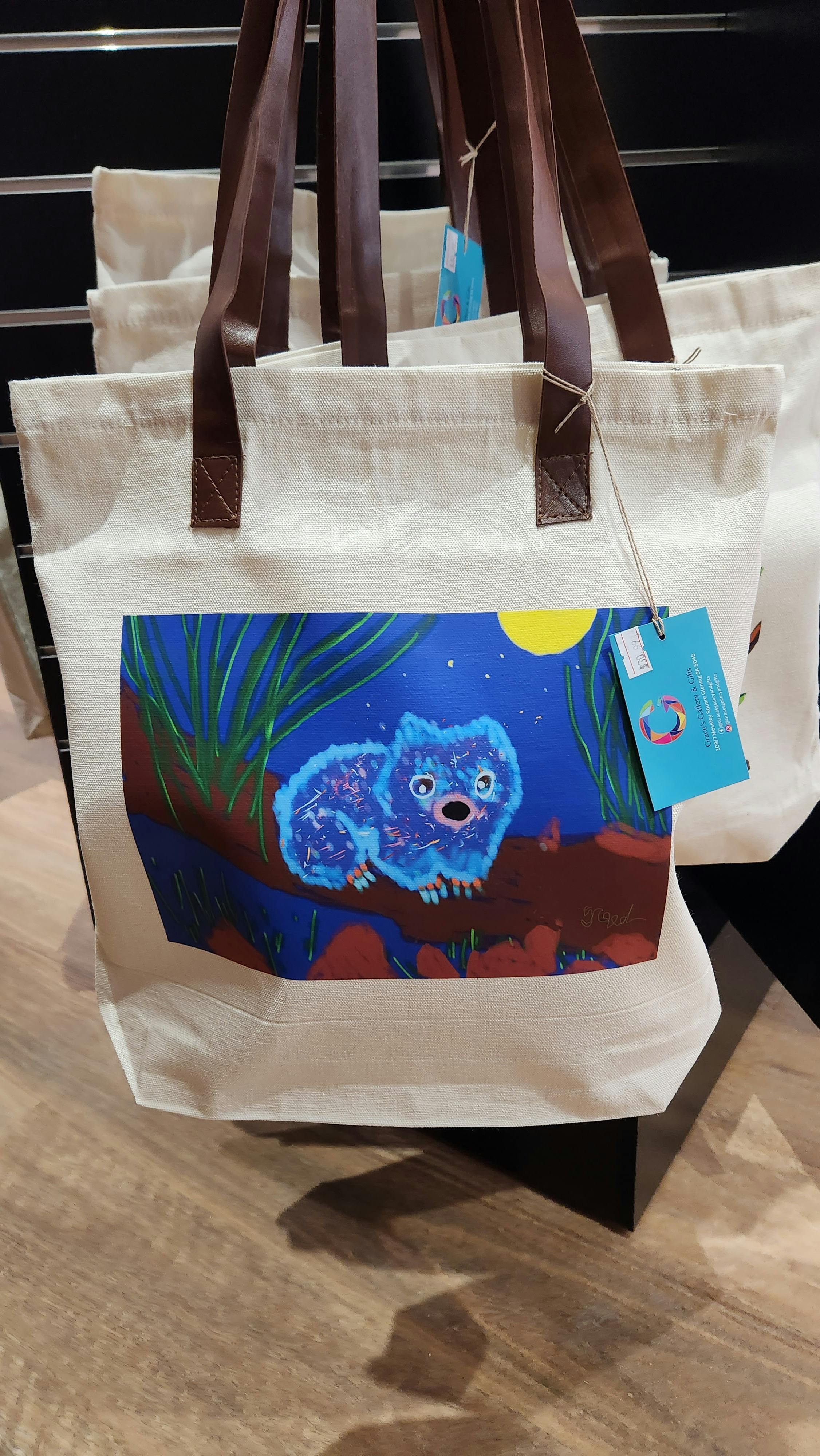 A tote bag with wombat design . the tote bag has white background and brown handle.