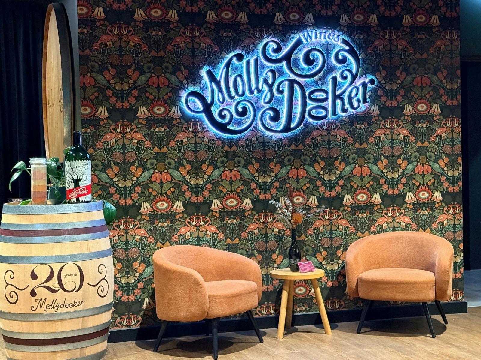 The Mollydooker logo lit up on the entrance wall with wine bottles on a wine barrel nearby