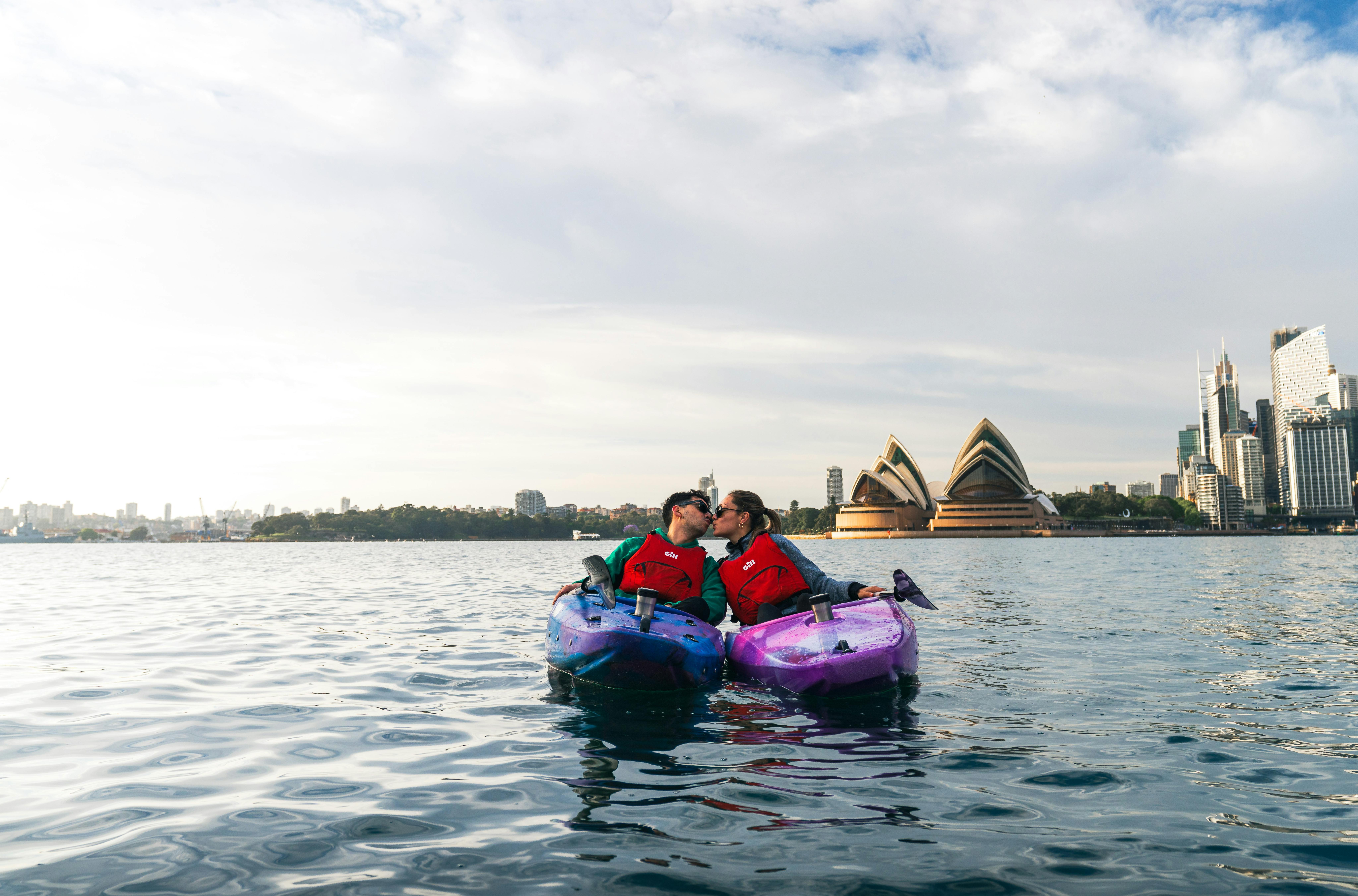 Couple kiss with the iconic Sydney Opera House behind them with Sydney By Kayak.