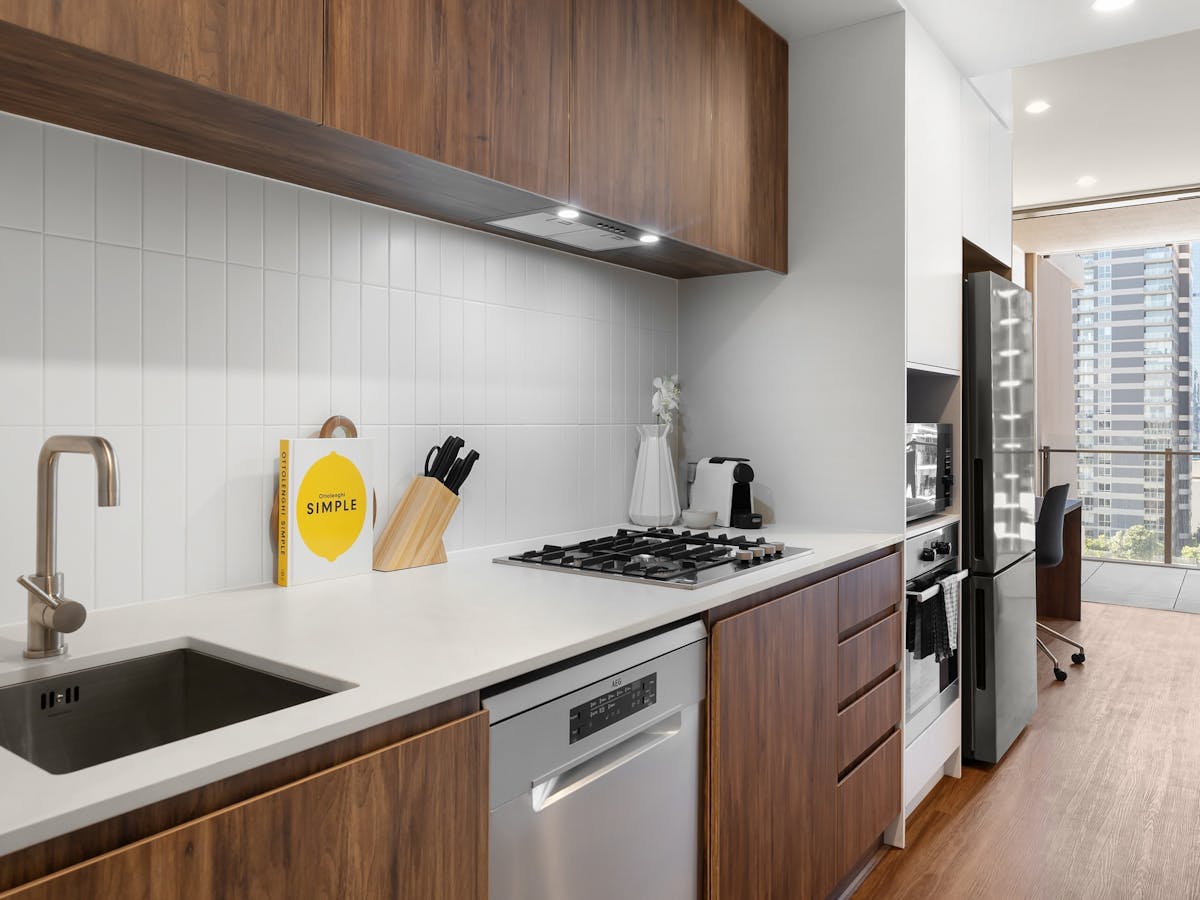 Modern kichen with white benchtop, sink, stainless steel dishwasher and wooden cabinetry.