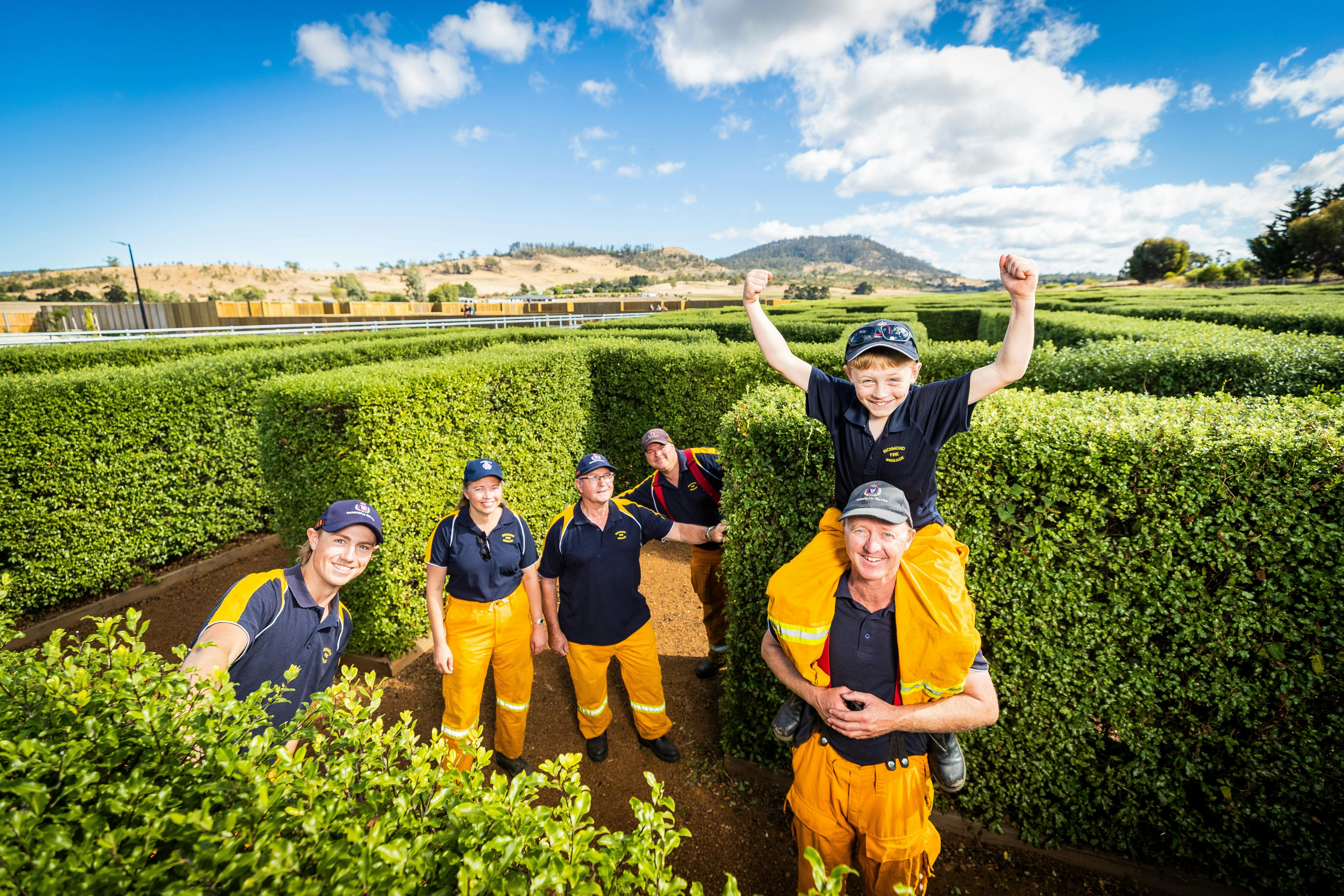 Team of volunteer firefighters. Young boy with his arms in the air,  sits on the shoulders of a man