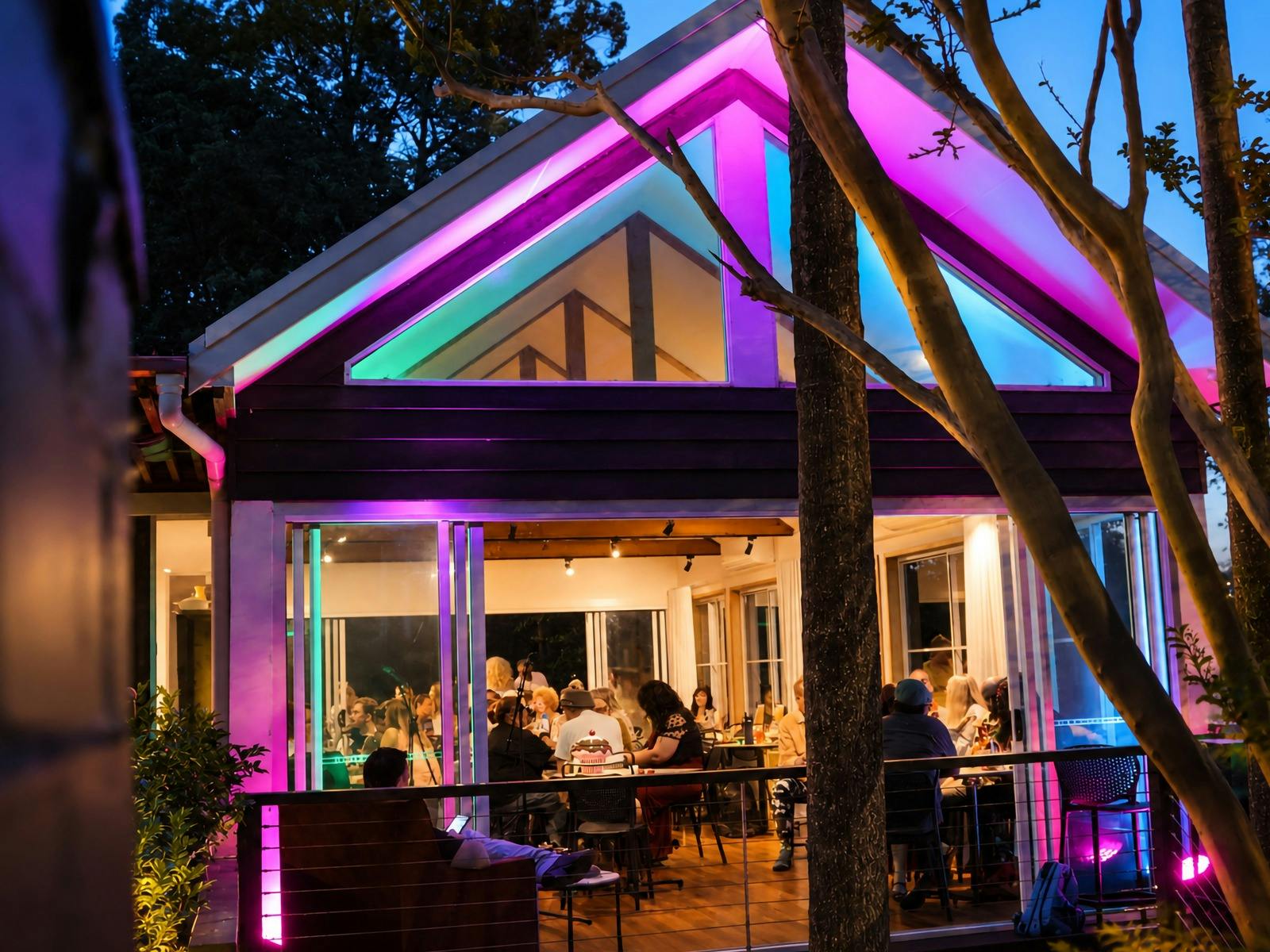 BridgeHaus at dusk, with pink and blue lighting around the peaked roof and guests seated inside.