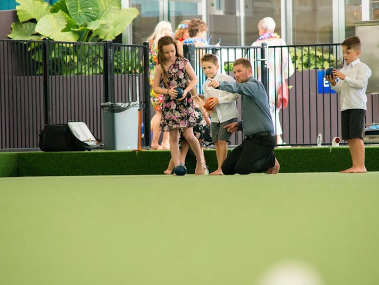 Image of a young family playing barefoot bowls. Father, 2 sons and a daughter