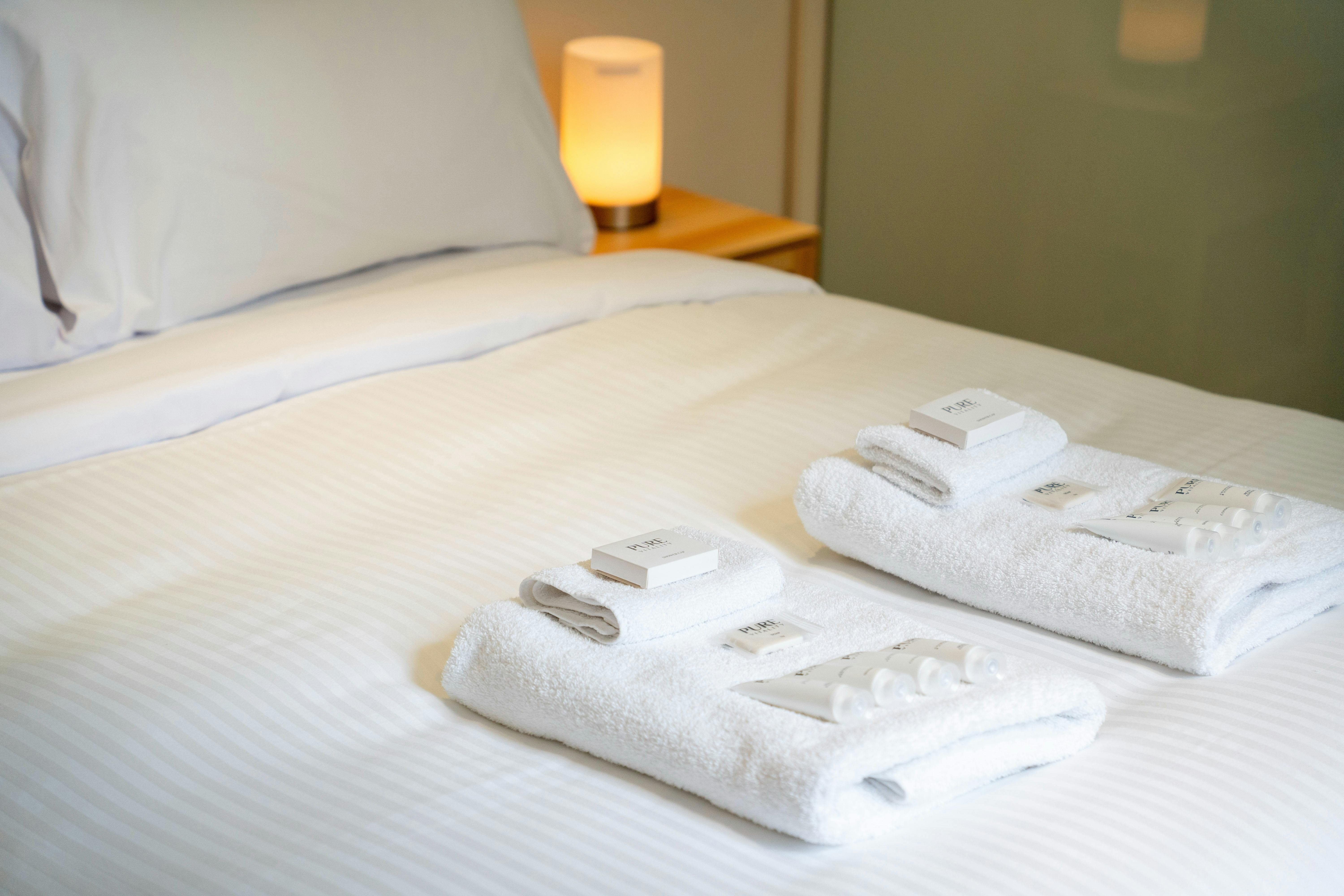Neatly arranged bed with fresh towels and luxury bathroom products.