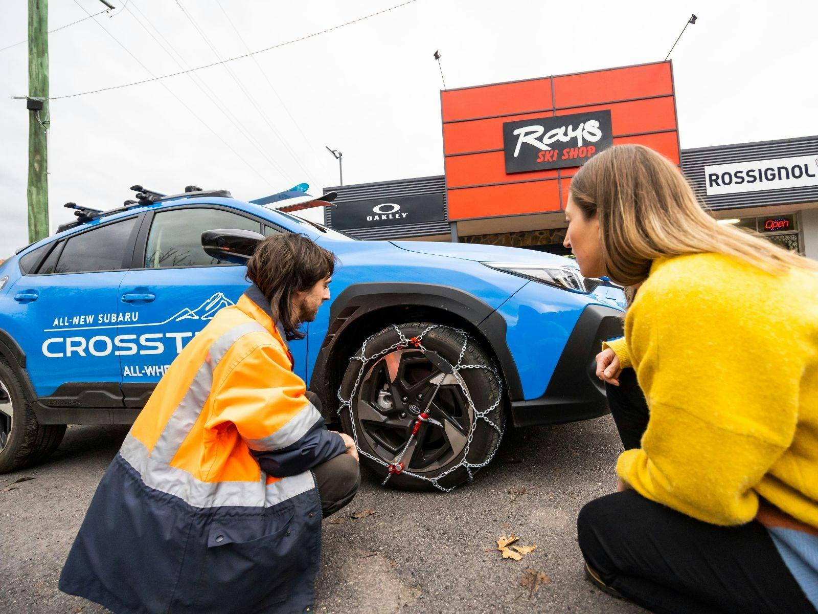 Staff member and guest testing chains on vehicle at Ray's Ski Hire