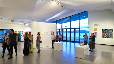 People attend an exhibition in a spacious gallery, with large windows looking on to the lake.