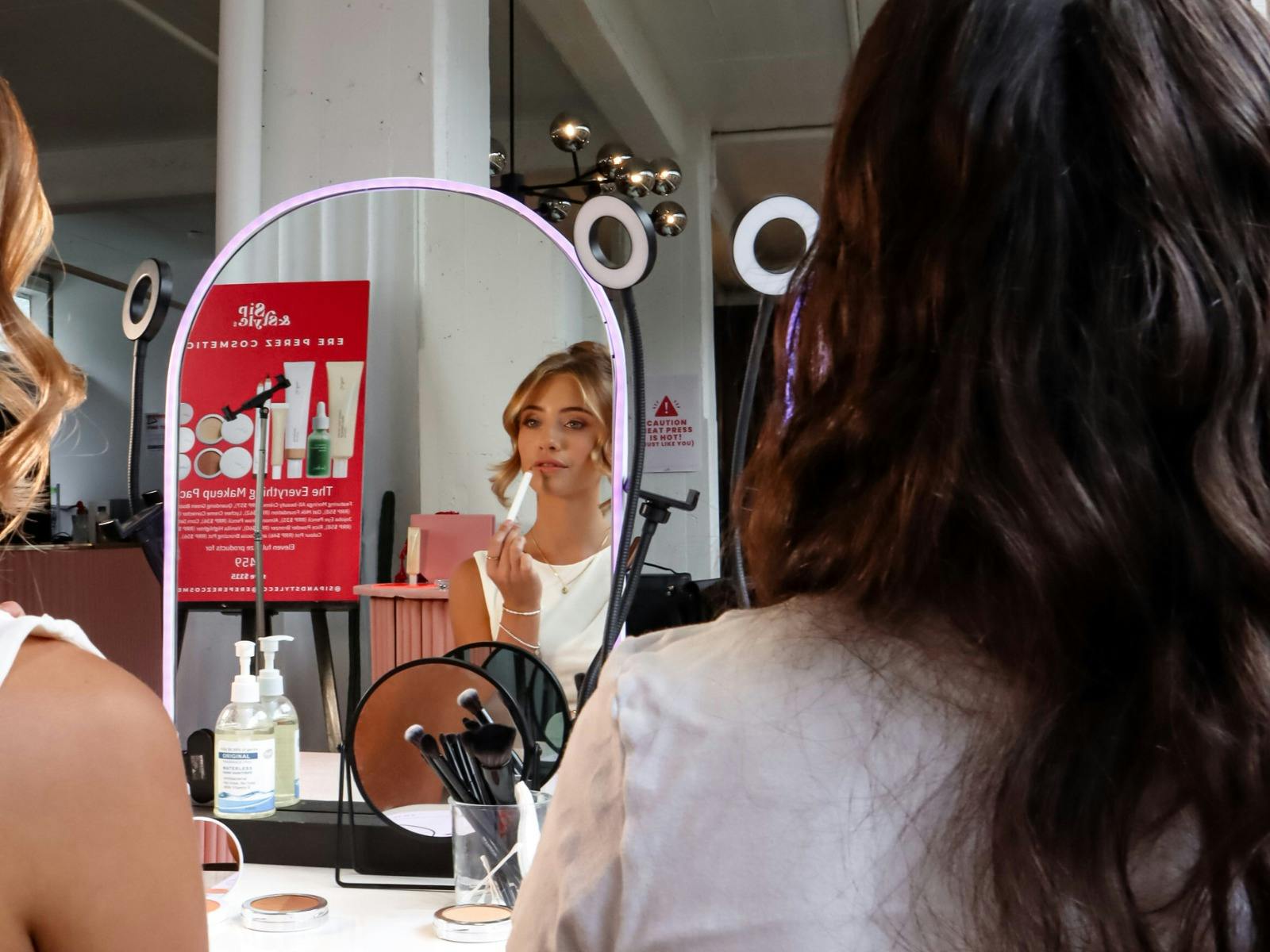 Woman applying lipstick at a lighted mirror during a makeup session in a modern beauty studio.