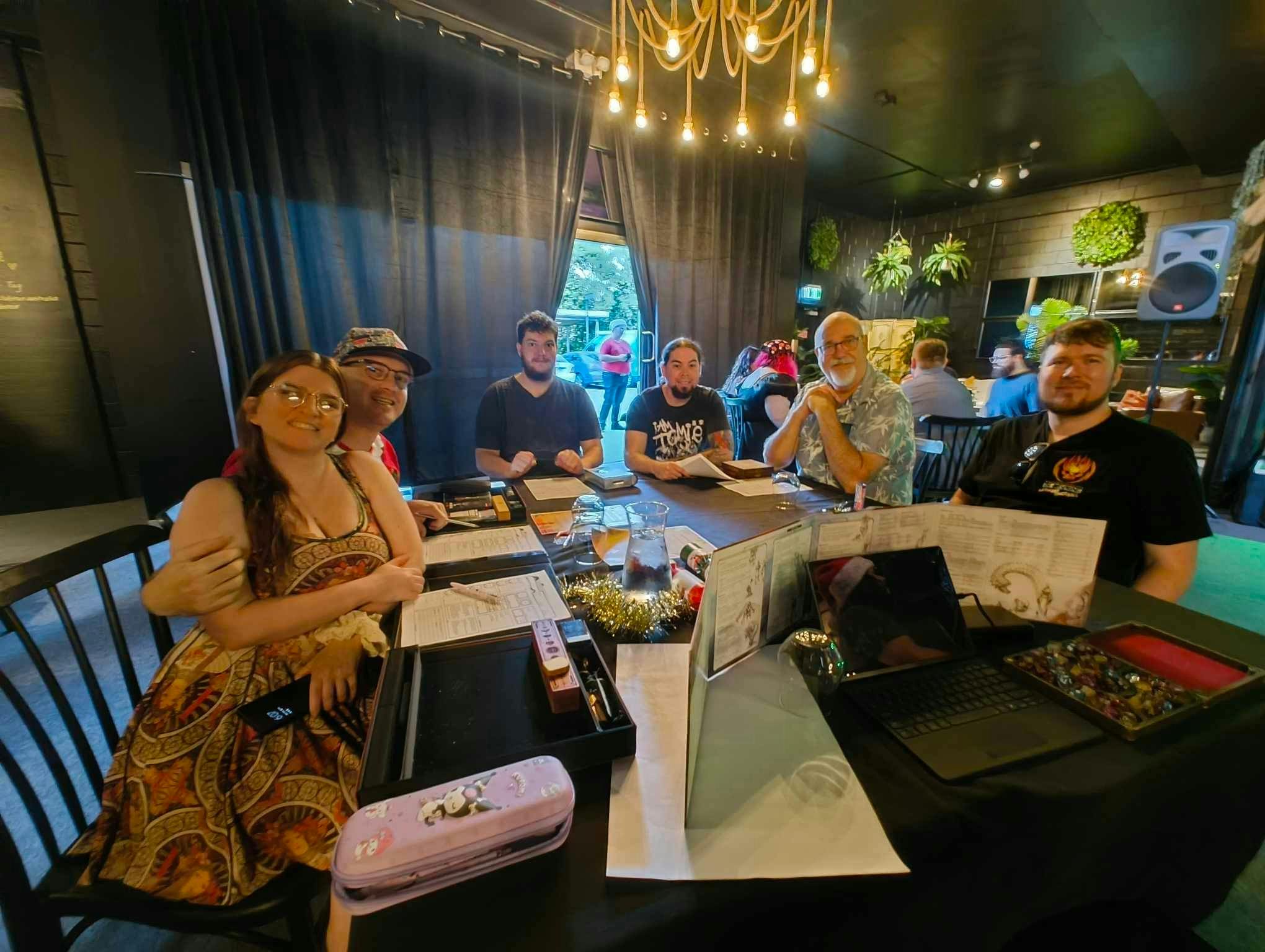 A table full of D&D player photo is taken frombehind a DM's screen with all players smiling