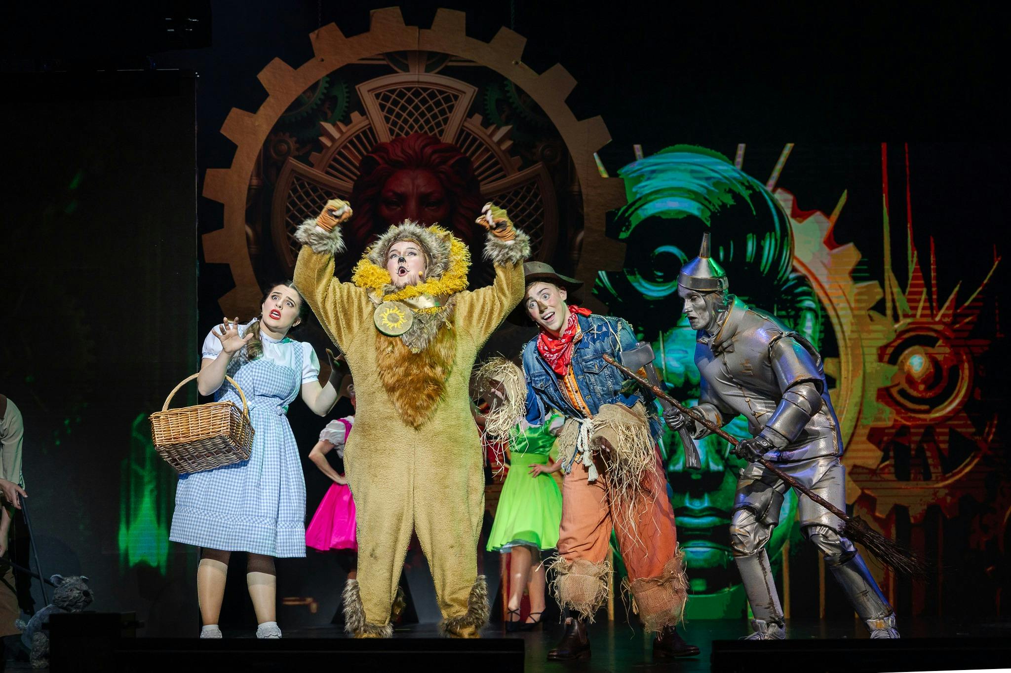 Pantomime cast in colourful costumes, including a lion, scarecrow and tin man, on stage