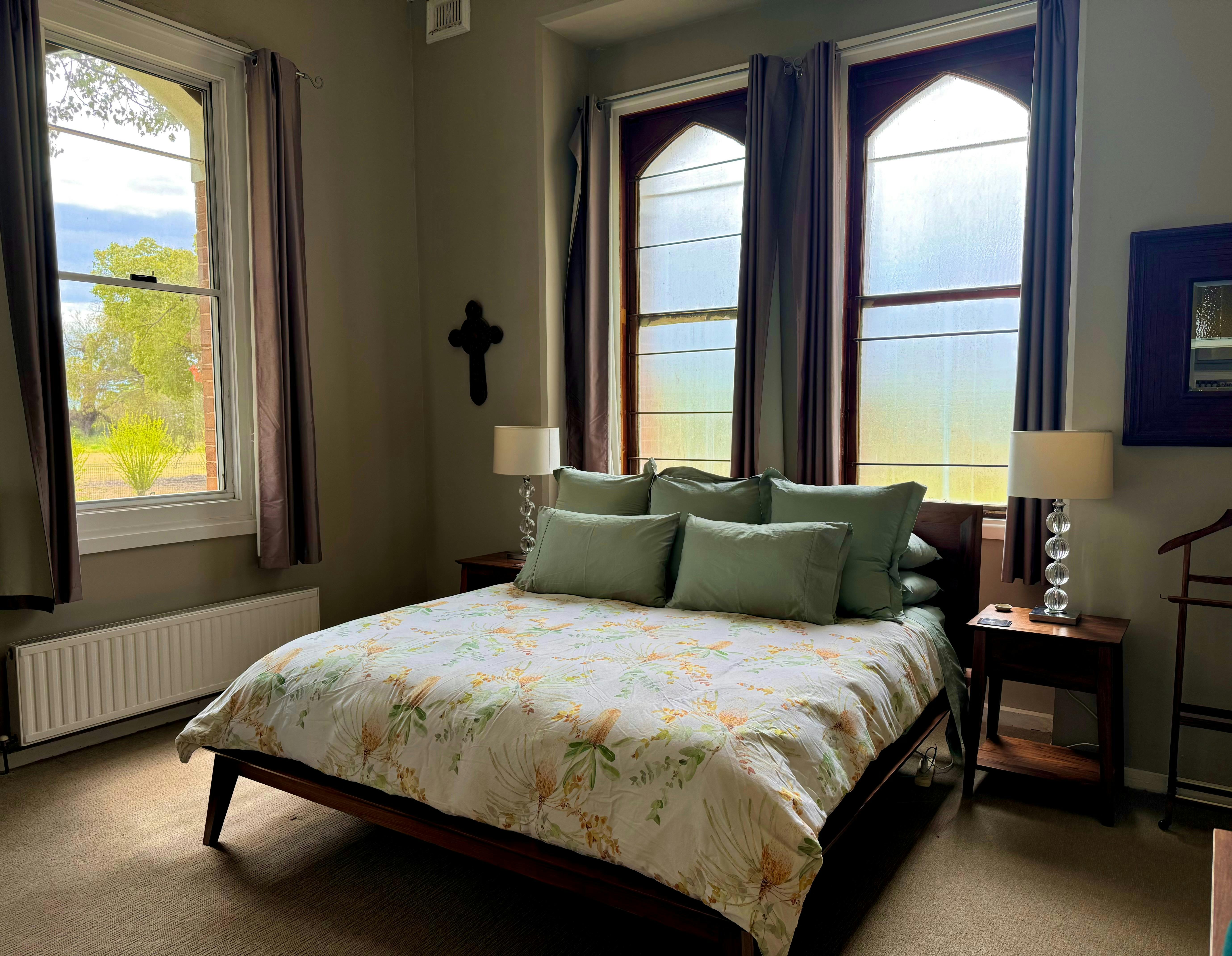 A king sized bed with green pillows and two gothic arched windows