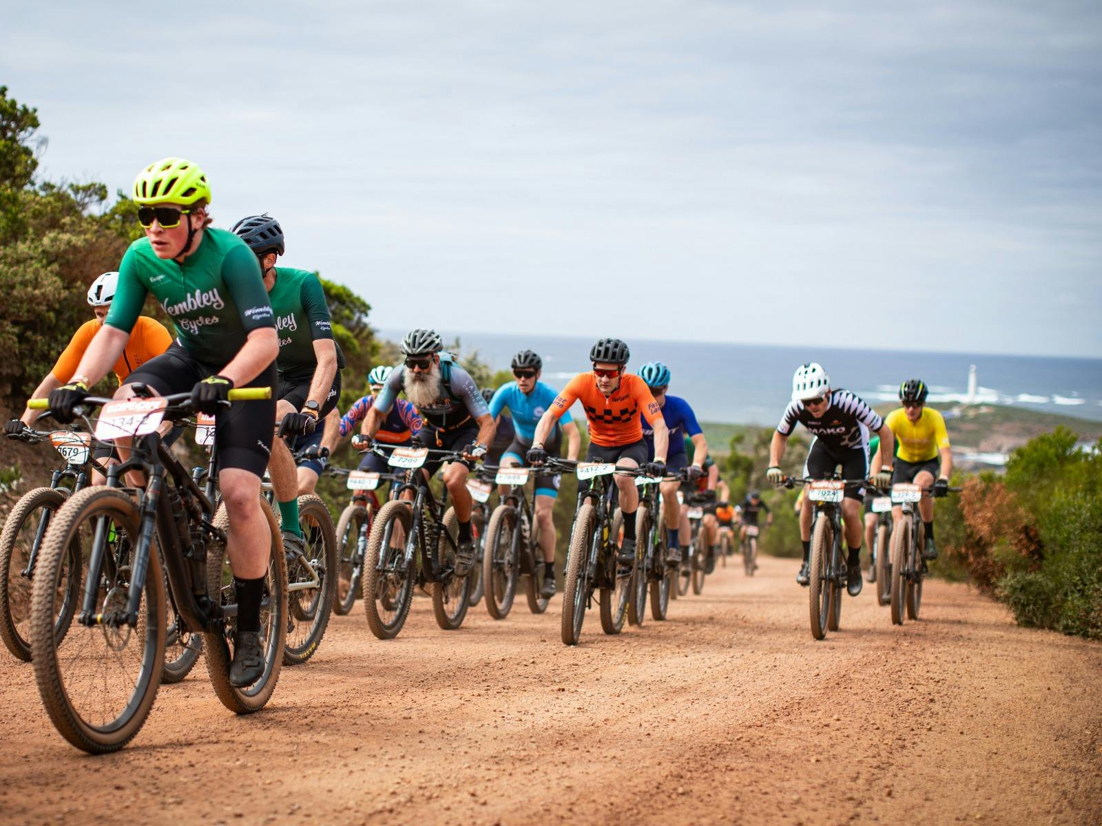 Mountain bike group racing up red gravel road, with coast in background