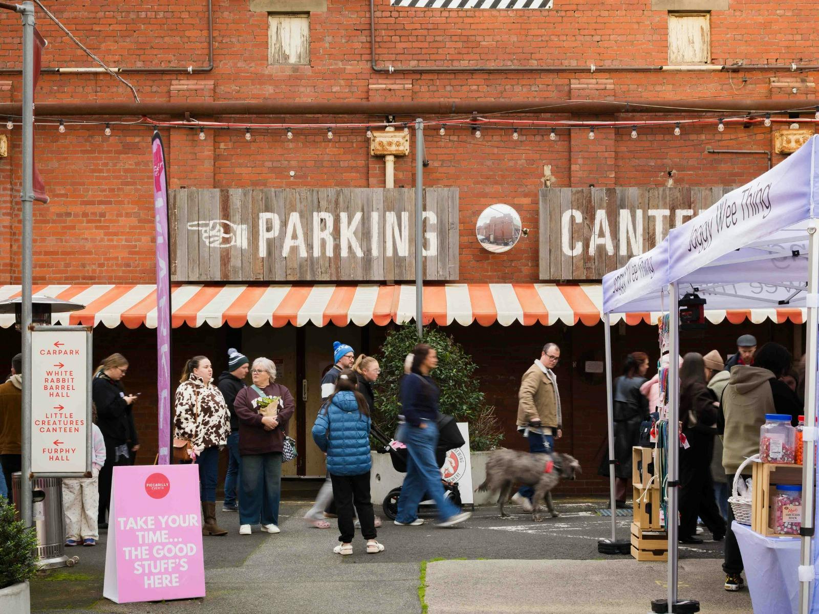 Crowds browsing outdoor market stalls in a red-brick brewery precinct.