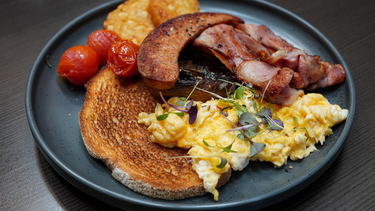A breakfast order with bacon, sausage, scrambled eggs, hash browns, tomatoes and toast