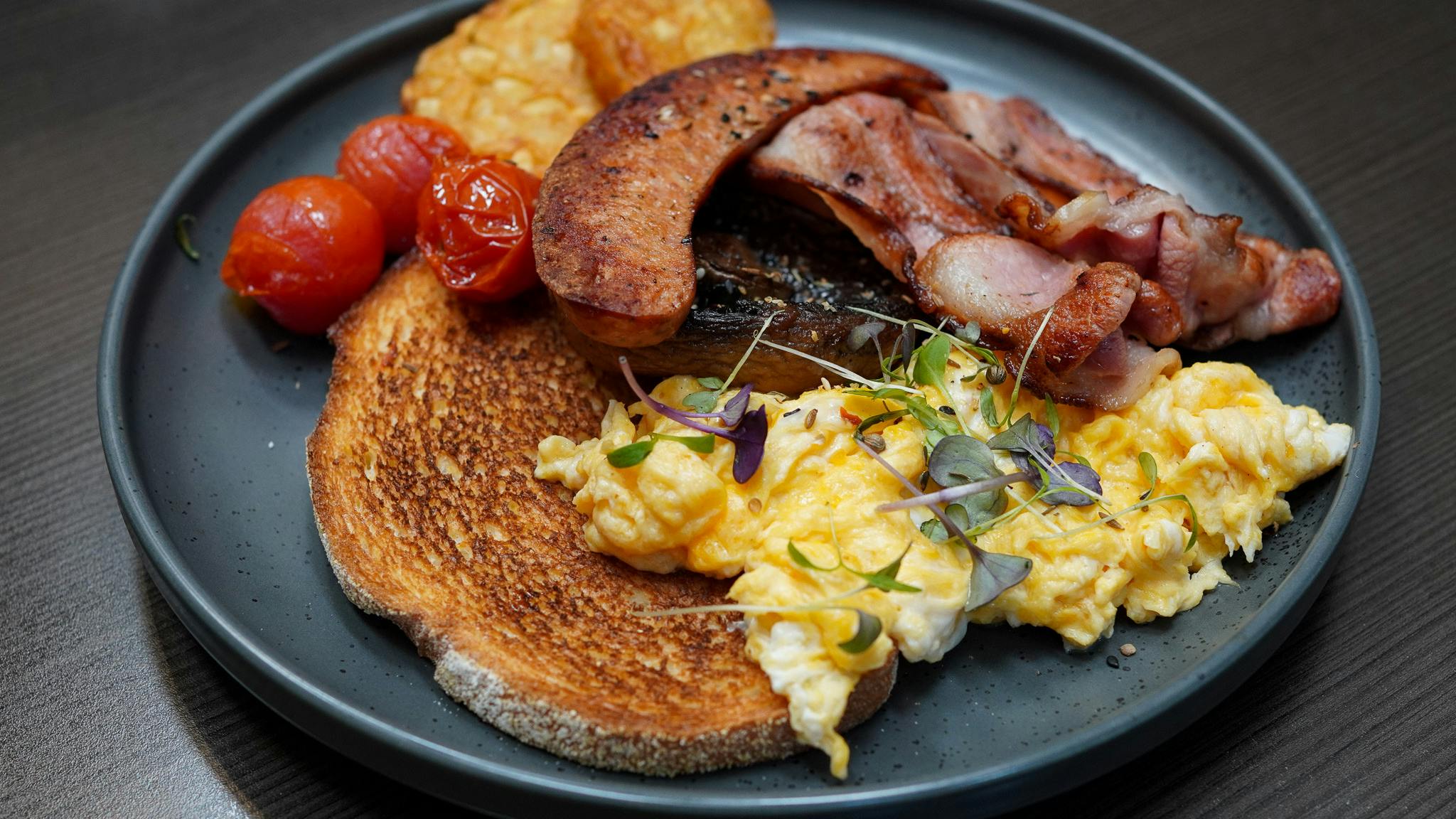 A breakfast order with bacon, sausage, scrambled eggs, hash browns, tomatoes and toast A breakfast order with bacon, sausage, scrambled eggs, hash browns, tomatoes and toast
