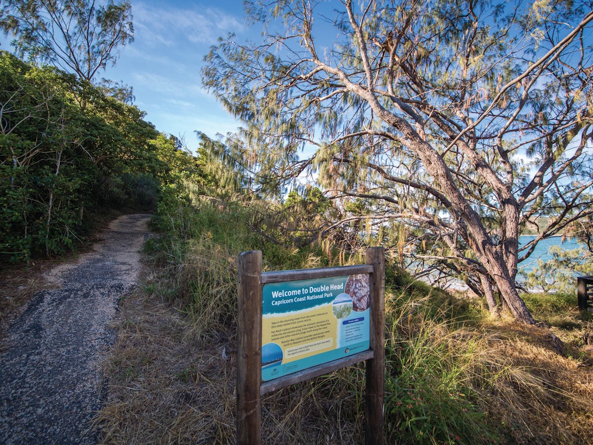 Sealed track with park welcome sign surrounded by coastal vegetation Sealed track with park welcome sign surrounded by coastal vegetation