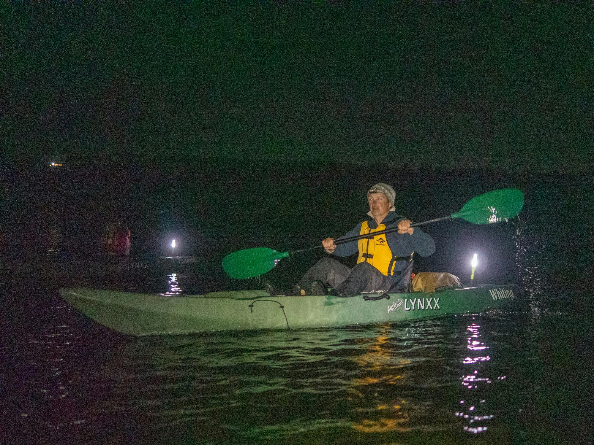 A kayaker paddling at night with a safety light glowing on the back of the kayak.