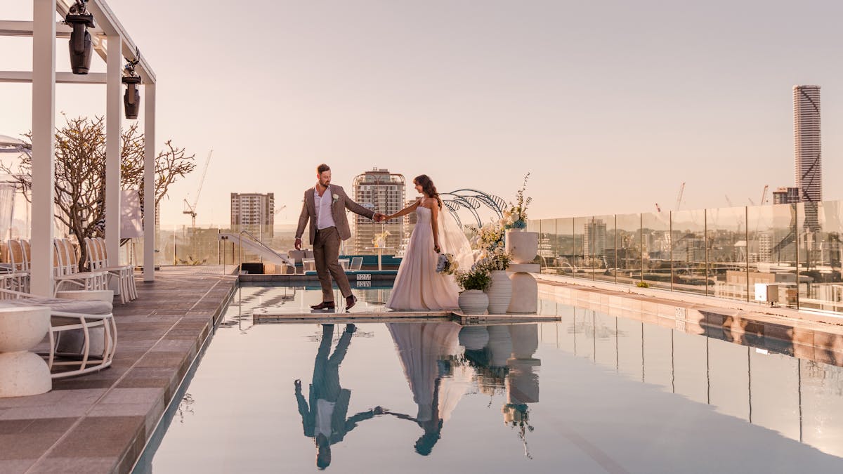 A wedding event at Lina Rooftop with a couple standing over the pool with stunning views of Brisbane