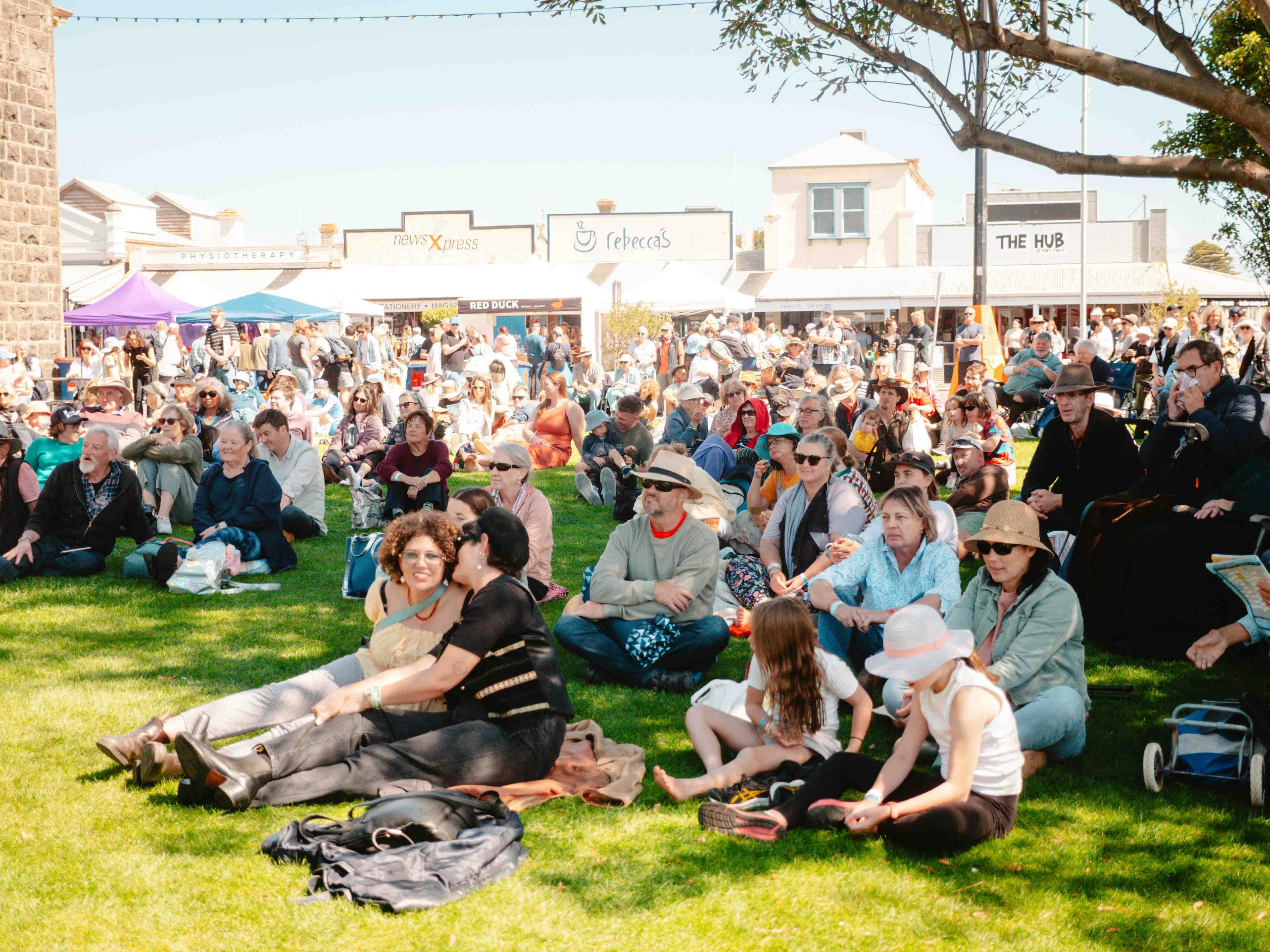 Many people sit on a grassed area in the town of Port Fairy to watch music.