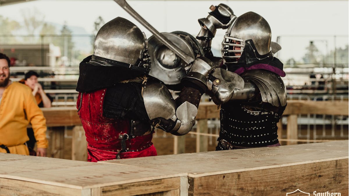 Two knights in full armor clashing with swords during a 1v1 Buhurt match.