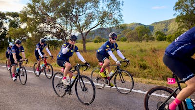 Cyclists riding on the road in a peloton with grass and hills scenic background