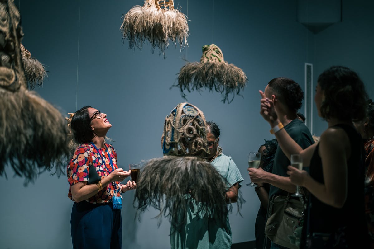 A group of people stand in the gallery surrounded by hanging woven works with emu features.