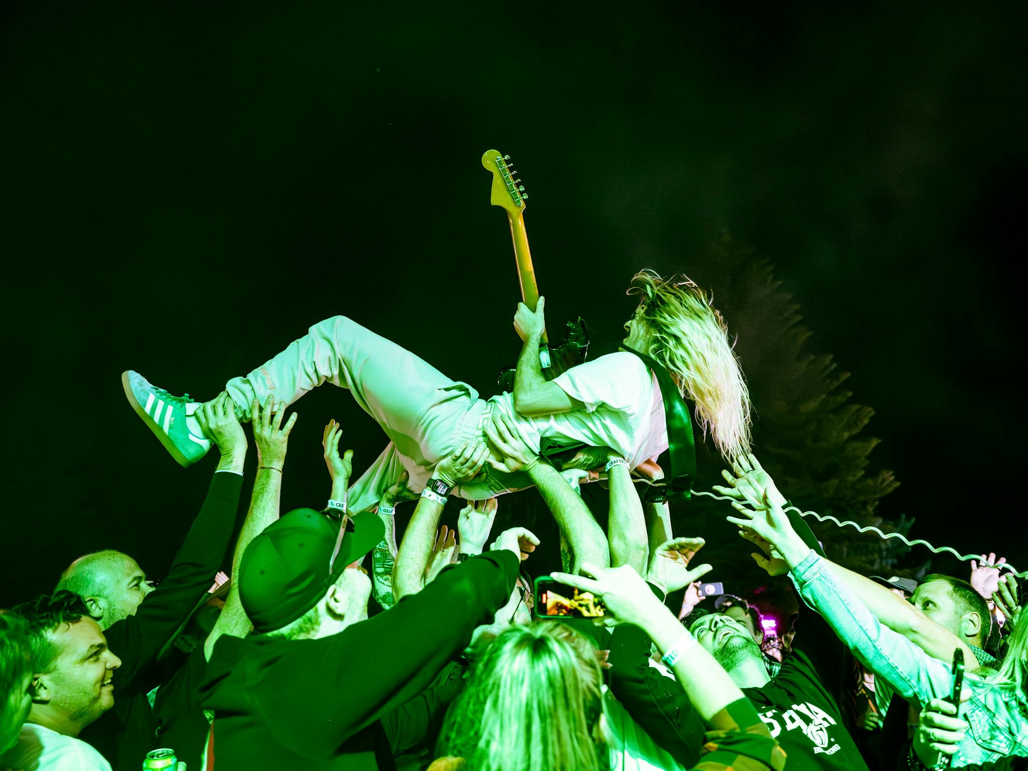 A man holding a guitar crowd surfs at the festival